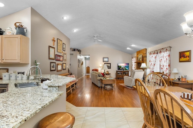 kitchen featuring ceiling fan, lofted ceiling, sink, and light stone counters