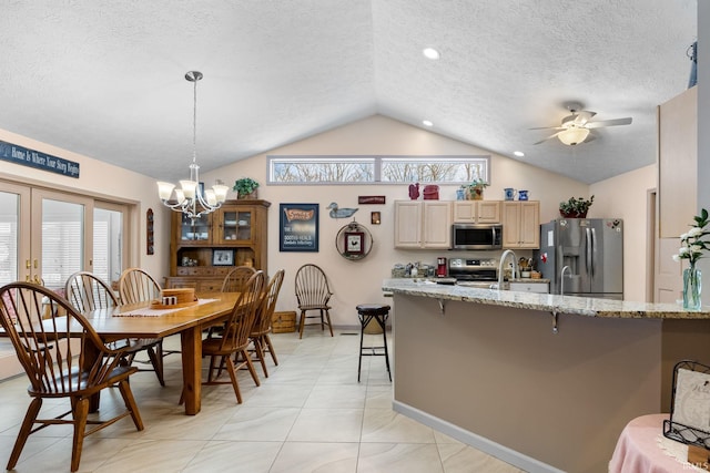 kitchen with a breakfast bar, vaulted ceiling, appliances with stainless steel finishes, light stone countertops, and ceiling fan with notable chandelier