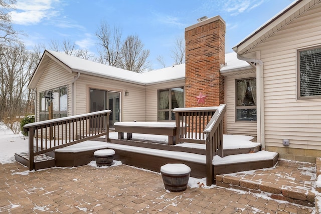 snow covered rear of property featuring a wooden deck and a patio area