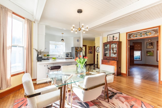 dining room featuring a notable chandelier, beam ceiling, sink, and light wood-type flooring