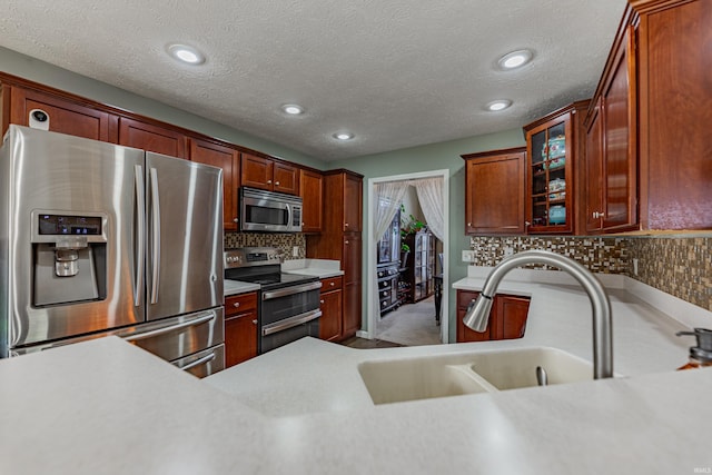 kitchen featuring stainless steel appliances, sink, backsplash, and a textured ceiling