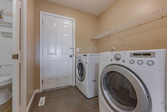 clothes washing area with a textured ceiling, washer and clothes dryer, and dark tile patterned floors