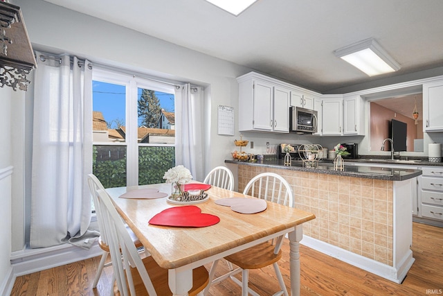 kitchen featuring white cabinetry, sink, dark stone counters, kitchen peninsula, and light wood-type flooring