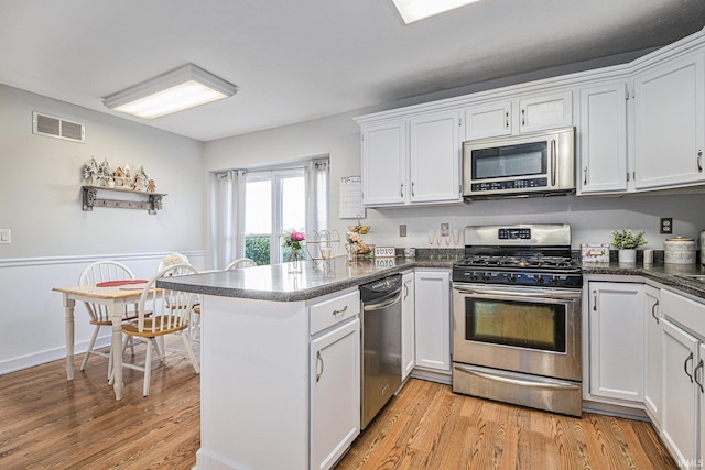 kitchen with appliances with stainless steel finishes, kitchen peninsula, light wood-type flooring, and white cabinets