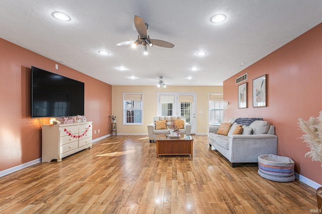 living room with ceiling fan, light hardwood / wood-style flooring, and a textured ceiling