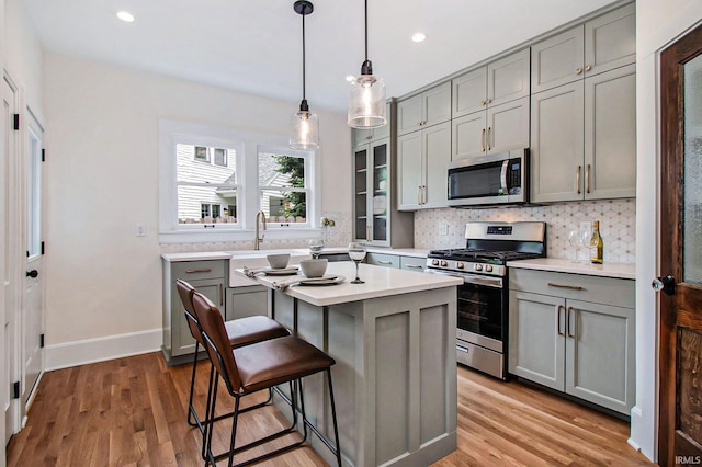 kitchen featuring gray cabinets, a breakfast bar area, decorative backsplash, a center island, and stainless steel appliances