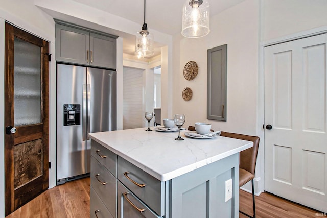 kitchen with pendant lighting, stainless steel fridge, gray cabinets, light hardwood / wood-style flooring, and a kitchen island