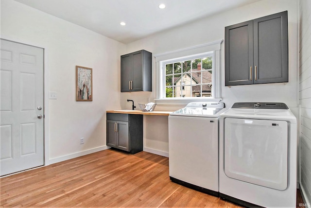 laundry room with cabinets, washer and dryer, sink, and light hardwood / wood-style flooring