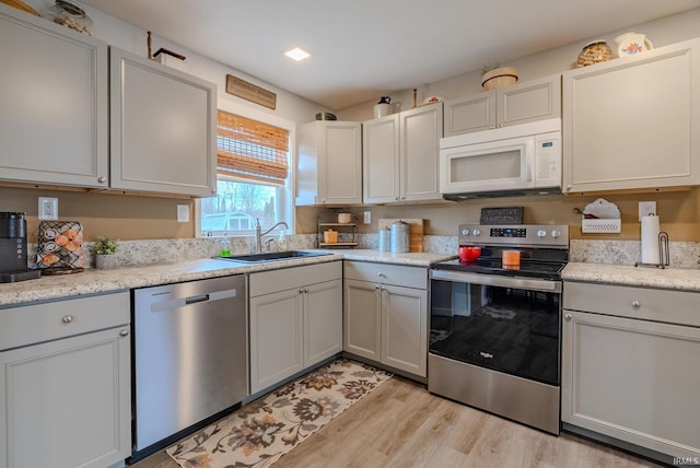 kitchen featuring light stone countertops, appliances with stainless steel finishes, sink, and light wood-type flooring