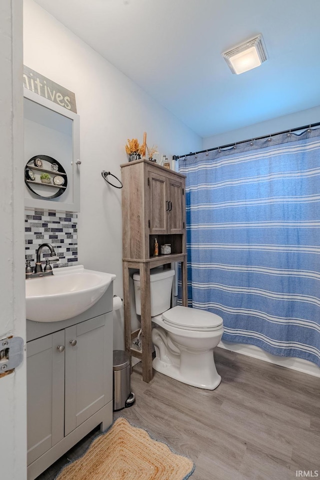 bathroom featuring hardwood / wood-style floors, backsplash, vanity, toilet, and walk in shower