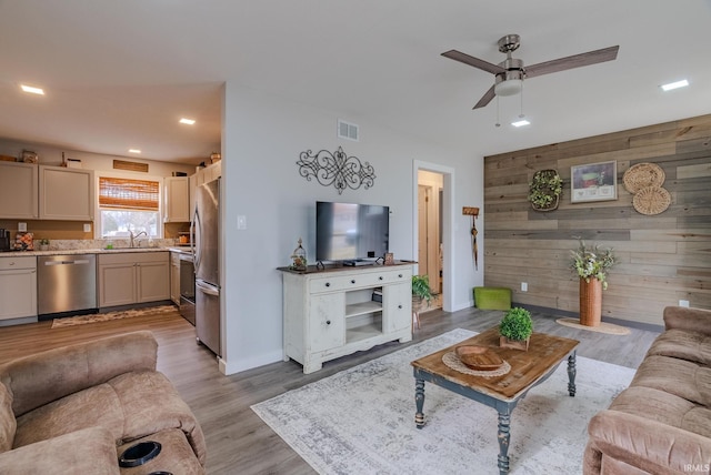 living room featuring ceiling fan, sink, light hardwood / wood-style floors, and wood walls