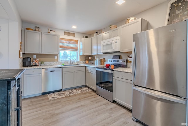 kitchen with sink, white cabinetry, stainless steel appliances, light hardwood / wood-style floors, and light stone countertops