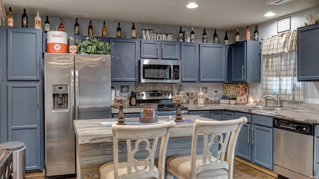 kitchen with blue cabinets, sink, light stone counters, appliances with stainless steel finishes, and hardwood / wood-style floors