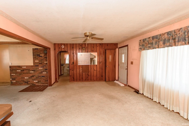 unfurnished living room featuring ceiling fan, light colored carpet, a textured ceiling, and wood walls