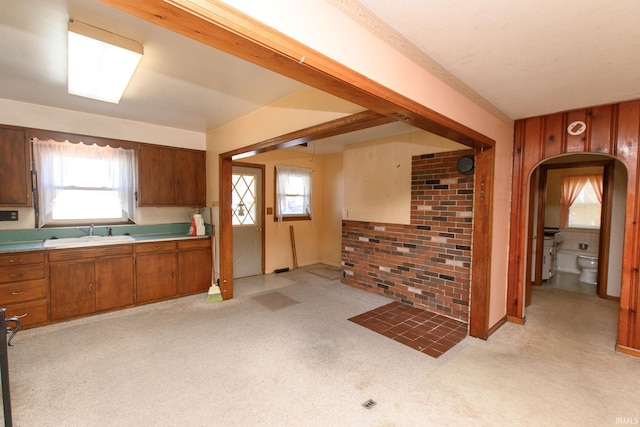 kitchen with sink, a wealth of natural light, light colored carpet, and brick wall