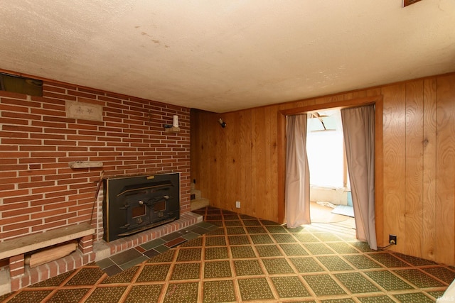 unfurnished living room with a wood stove, a textured ceiling, and wood walls