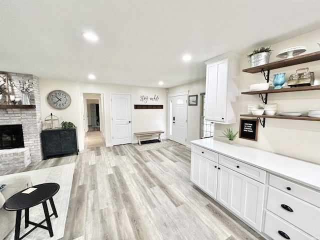 kitchen featuring light wood-type flooring, a brick fireplace, and white cabinets