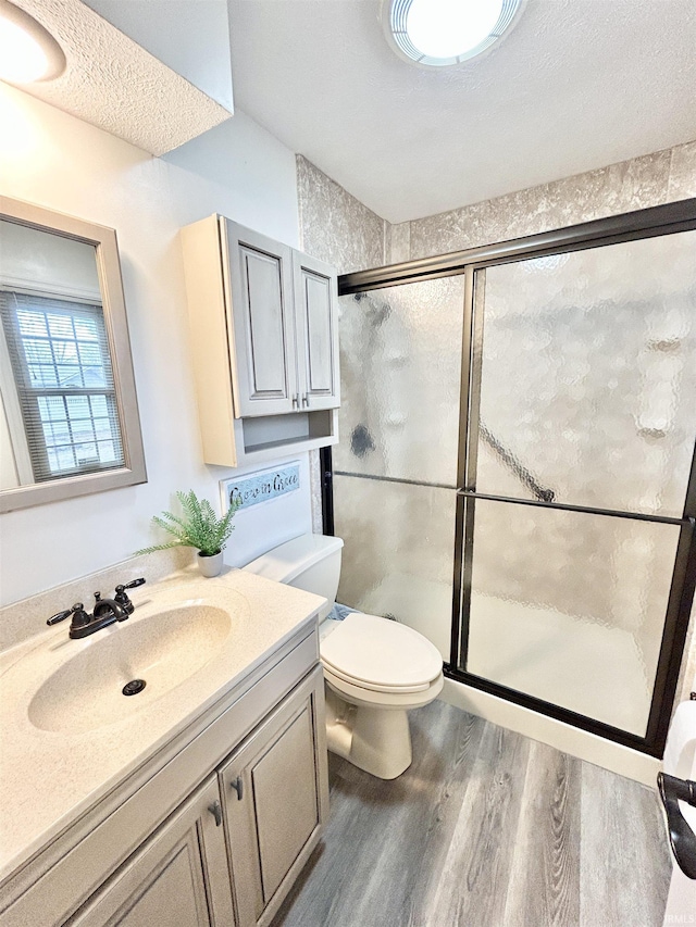 bathroom featuring hardwood / wood-style flooring, vanity, a textured ceiling, a shower with shower door, and toilet