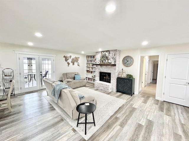 living room featuring a brick fireplace, light hardwood / wood-style flooring, and french doors