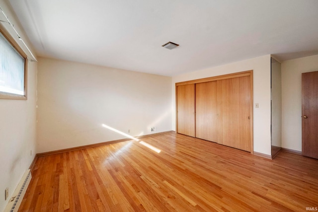 unfurnished bedroom with a closet, light hardwood / wood-style flooring, and a baseboard heating unit