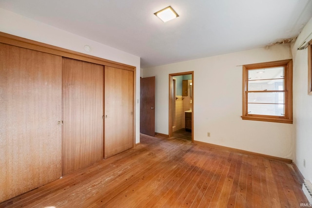 unfurnished bedroom with a baseboard radiator, ensuite bath, light hardwood / wood-style floors, and a closet