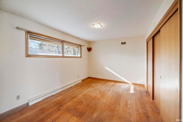 unfurnished bedroom with light hardwood / wood-style floors, a closet, and a baseboard heating unit