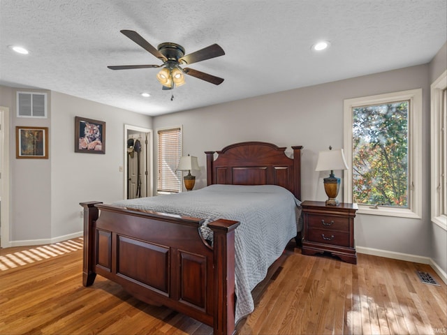 bedroom with ceiling fan, a walk in closet, light hardwood / wood-style floors, and a textured ceiling