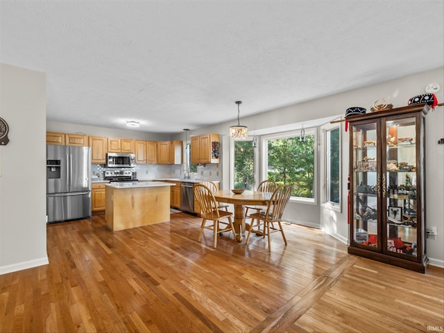 kitchen featuring light hardwood / wood-style flooring, decorative light fixtures, a kitchen island, and appliances with stainless steel finishes