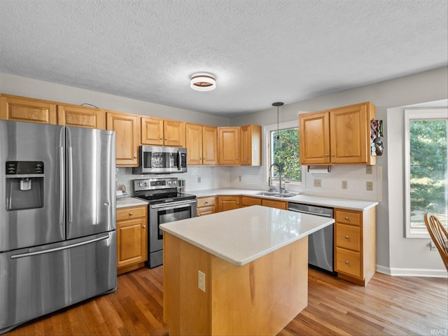 kitchen featuring appliances with stainless steel finishes, sink, hanging light fixtures, a center island, and light hardwood / wood-style floors