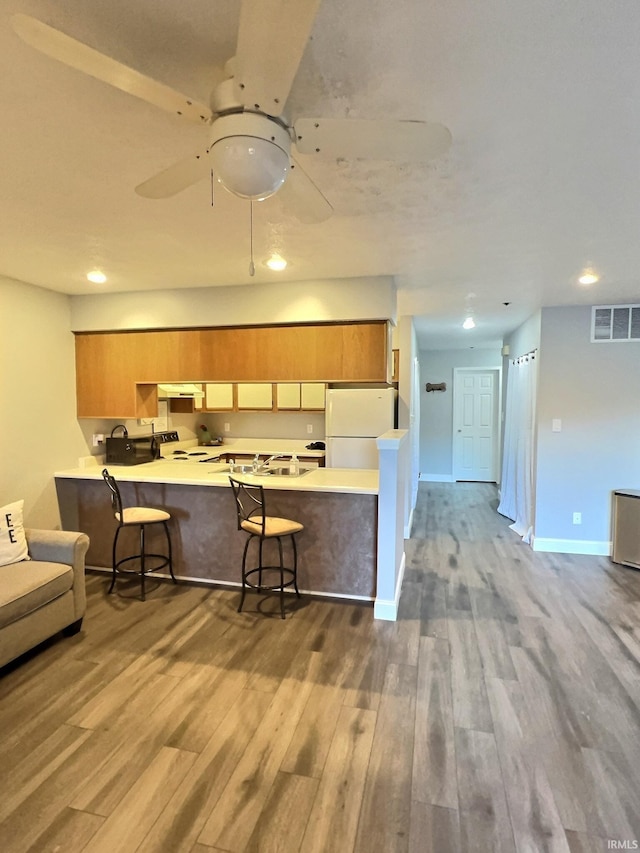 kitchen featuring a breakfast bar area, kitchen peninsula, wood-type flooring, and white fridge