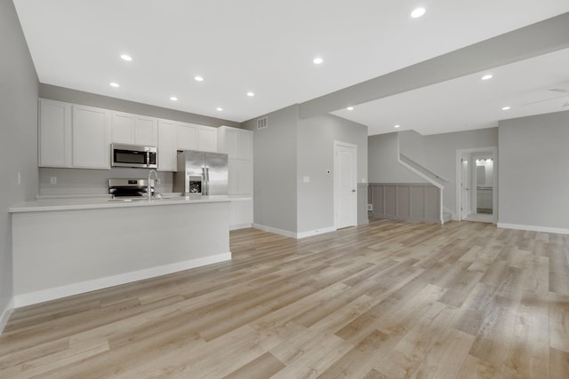 kitchen with white cabinetry, sink, kitchen peninsula, stainless steel appliances, and light hardwood / wood-style flooring