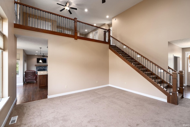 unfurnished living room featuring dark carpet, a fireplace, ceiling fan, and a high ceiling