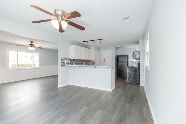 kitchen with white cabinetry, black refrigerator, dark hardwood / wood-style floors, kitchen peninsula, and backsplash