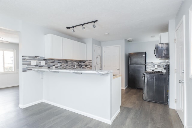 kitchen with dark wood-type flooring, a breakfast bar area, black refrigerator, white cabinets, and kitchen peninsula