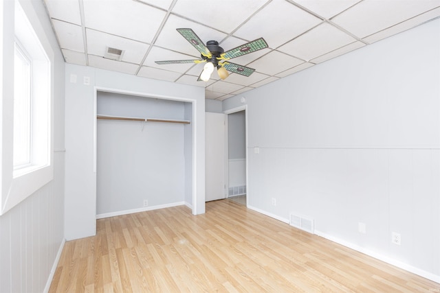 unfurnished bedroom featuring ceiling fan, a drop ceiling, light hardwood / wood-style floors, and a closet