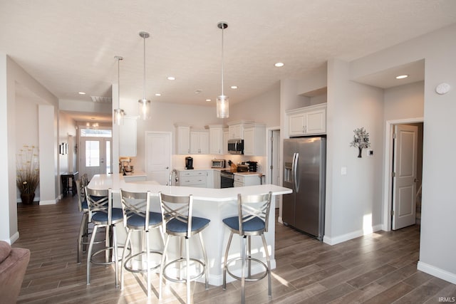 kitchen featuring dark wood-type flooring, hanging light fixtures, an island with sink, stainless steel appliances, and white cabinets