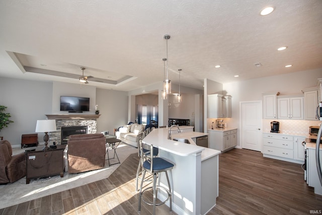 kitchen featuring sink, a kitchen breakfast bar, an island with sink, decorative light fixtures, and a raised ceiling