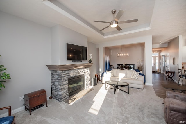 carpeted living room featuring a fireplace, a tray ceiling, and ceiling fan with notable chandelier