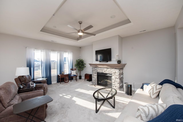 carpeted living room featuring a raised ceiling, ceiling fan, and a fireplace