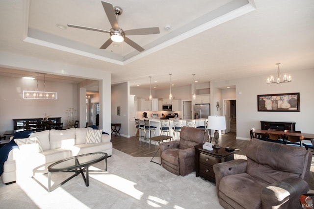 living room featuring a tray ceiling, light hardwood / wood-style flooring, ornamental molding, and ceiling fan with notable chandelier