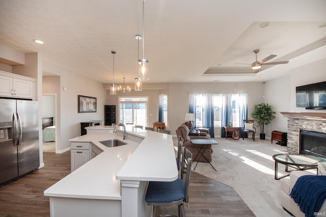 kitchen with pendant lighting, sink, white cabinets, a kitchen island with sink, and stainless steel refrigerator with ice dispenser