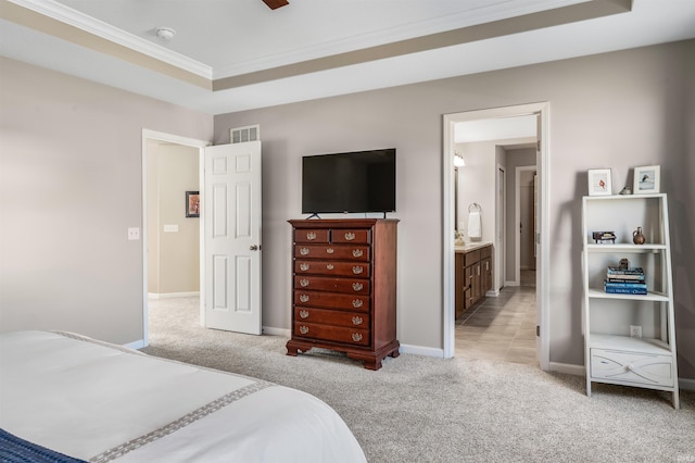 bedroom featuring a raised ceiling, ornamental molding, light colored carpet, and ensuite bath