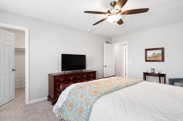 bedroom featuring a spacious closet, light carpet, and ceiling fan