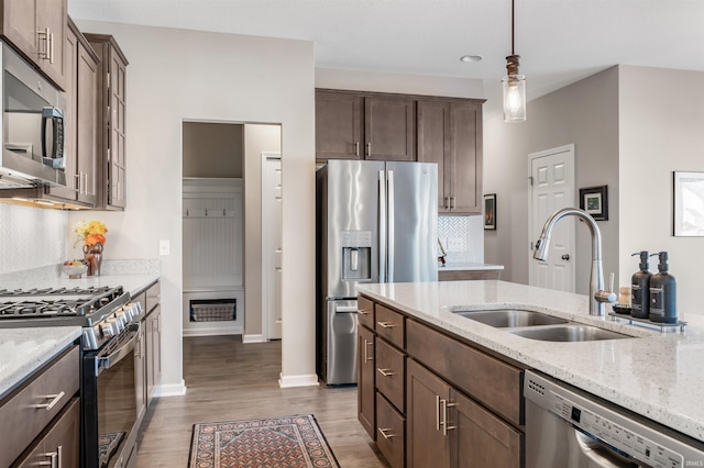 kitchen with decorative light fixtures, sink, light stone counters, stainless steel appliances, and dark brown cabinets