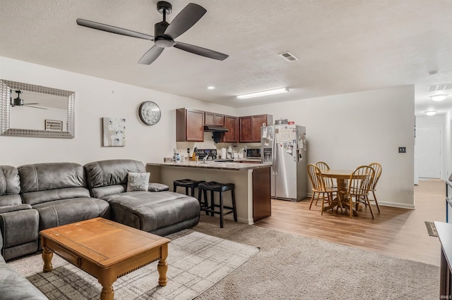 living room featuring ceiling fan, light hardwood / wood-style flooring, and a textured ceiling