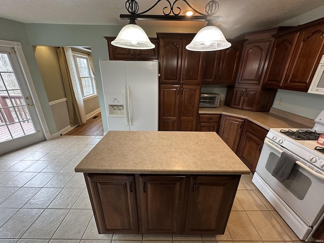 kitchen with pendant lighting, white appliances, a kitchen island, dark brown cabinetry, and light tile patterned flooring