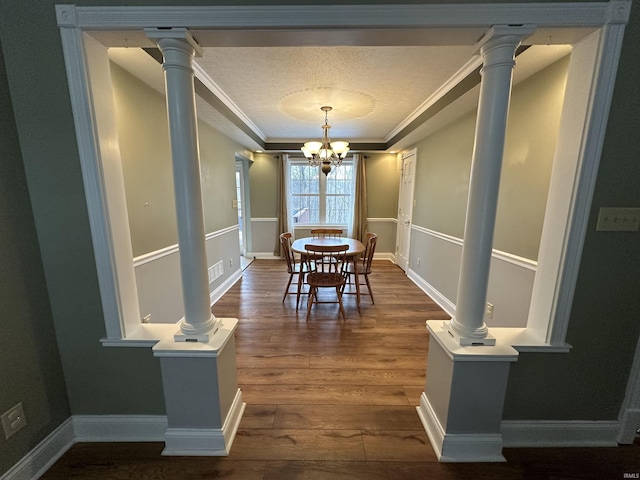 dining space featuring a chandelier, a textured ceiling, ornamental molding, dark hardwood / wood-style flooring, and decorative columns