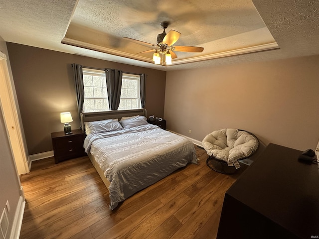 bedroom featuring a raised ceiling, a textured ceiling, and light wood-type flooring