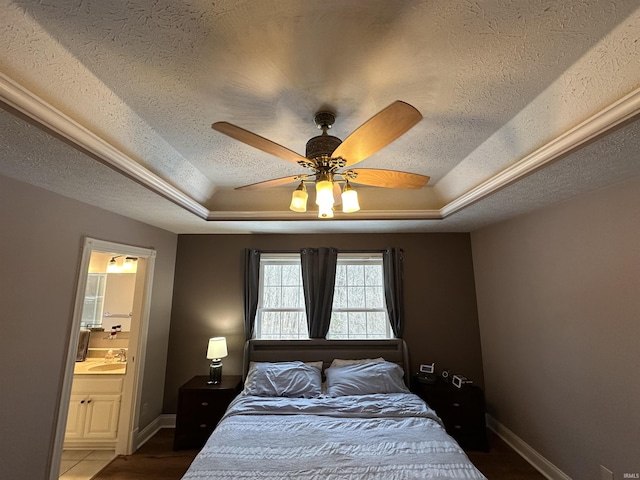 bedroom with connected bathroom, sink, a tray ceiling, and a textured ceiling