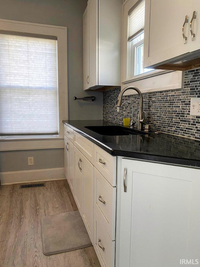 kitchen with tasteful backsplash, sink, white cabinets, and light wood-type flooring